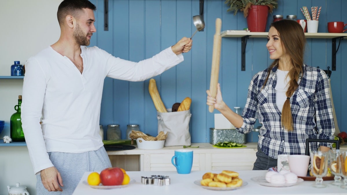 Happy couple having fun in the kitchen fencing with ladle and spoon while cooking breakfast at home in the morning